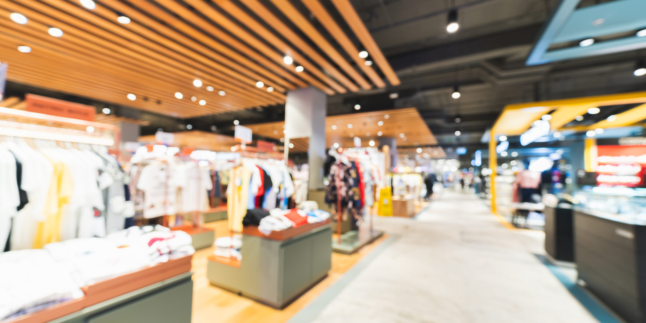 Blurred, defocused background of clothing shops in modern shopping mall or department store. Shopaholic lifestyle, or fashion dress outlet business concept