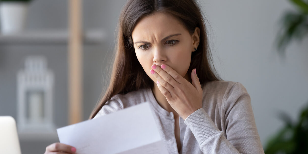Shocked stressed young woman reading document letter about debt