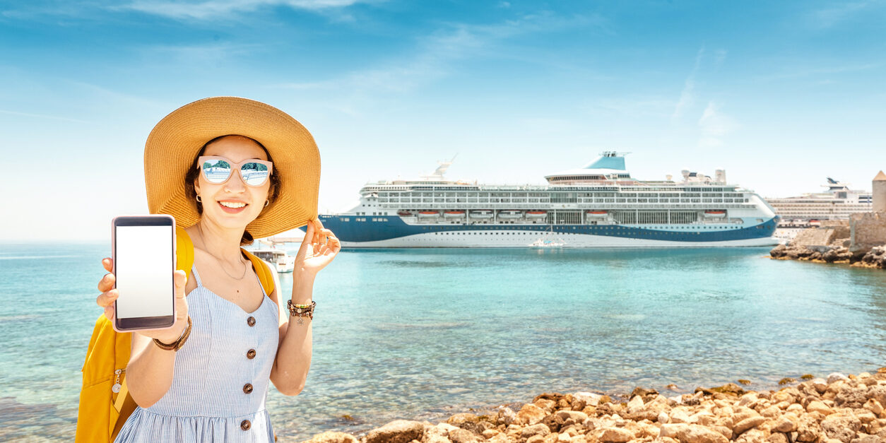 Asian woman traveler uses phone on the background of a large cruise liner. The concept of coverage, roaming and pay for the resort online