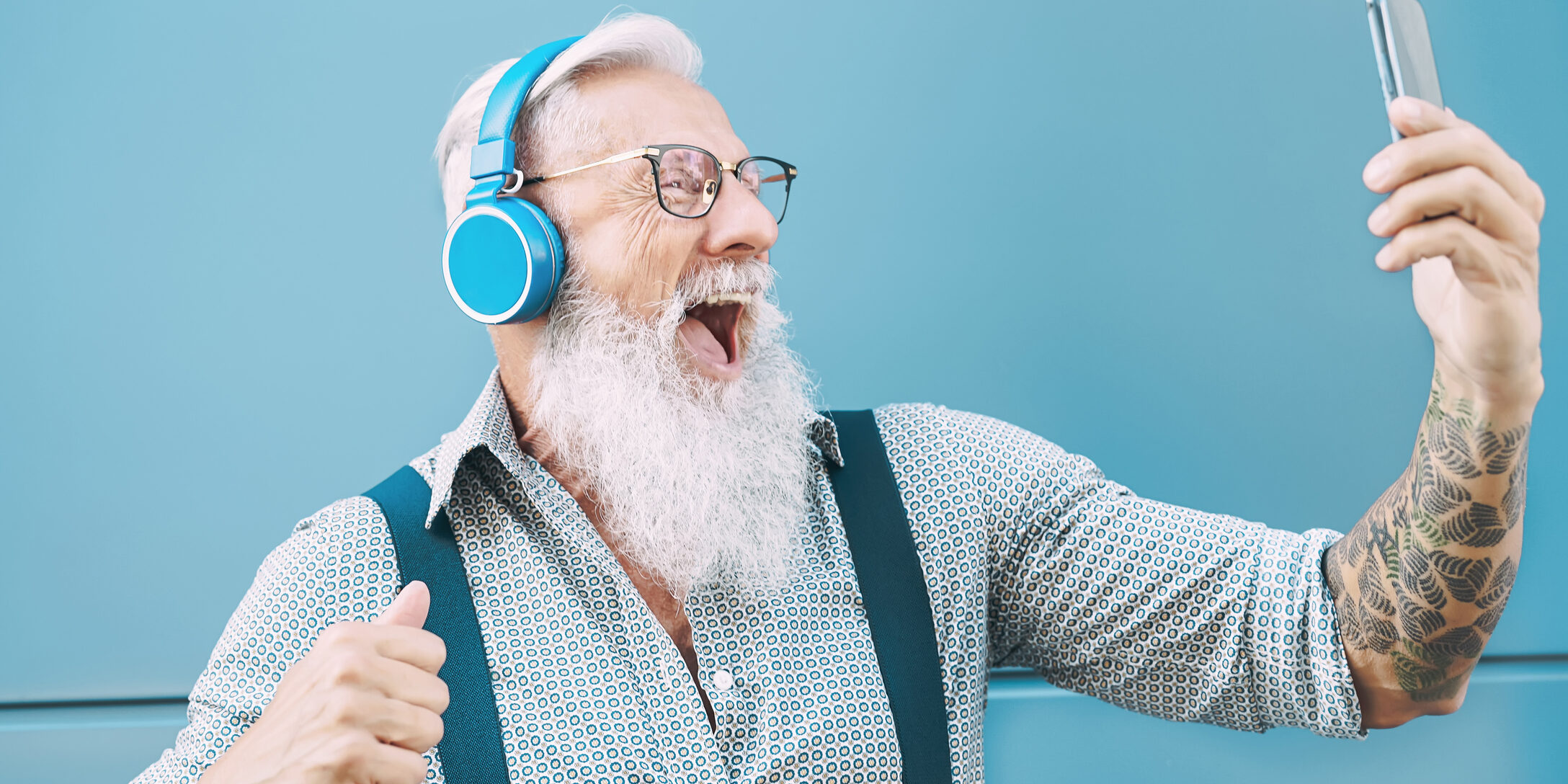 Happy senior man taking selfie while listening music with headphones – Hipster mature male having fun using mobile smartphone playlist apps – technology and elderly lifestyle people concept